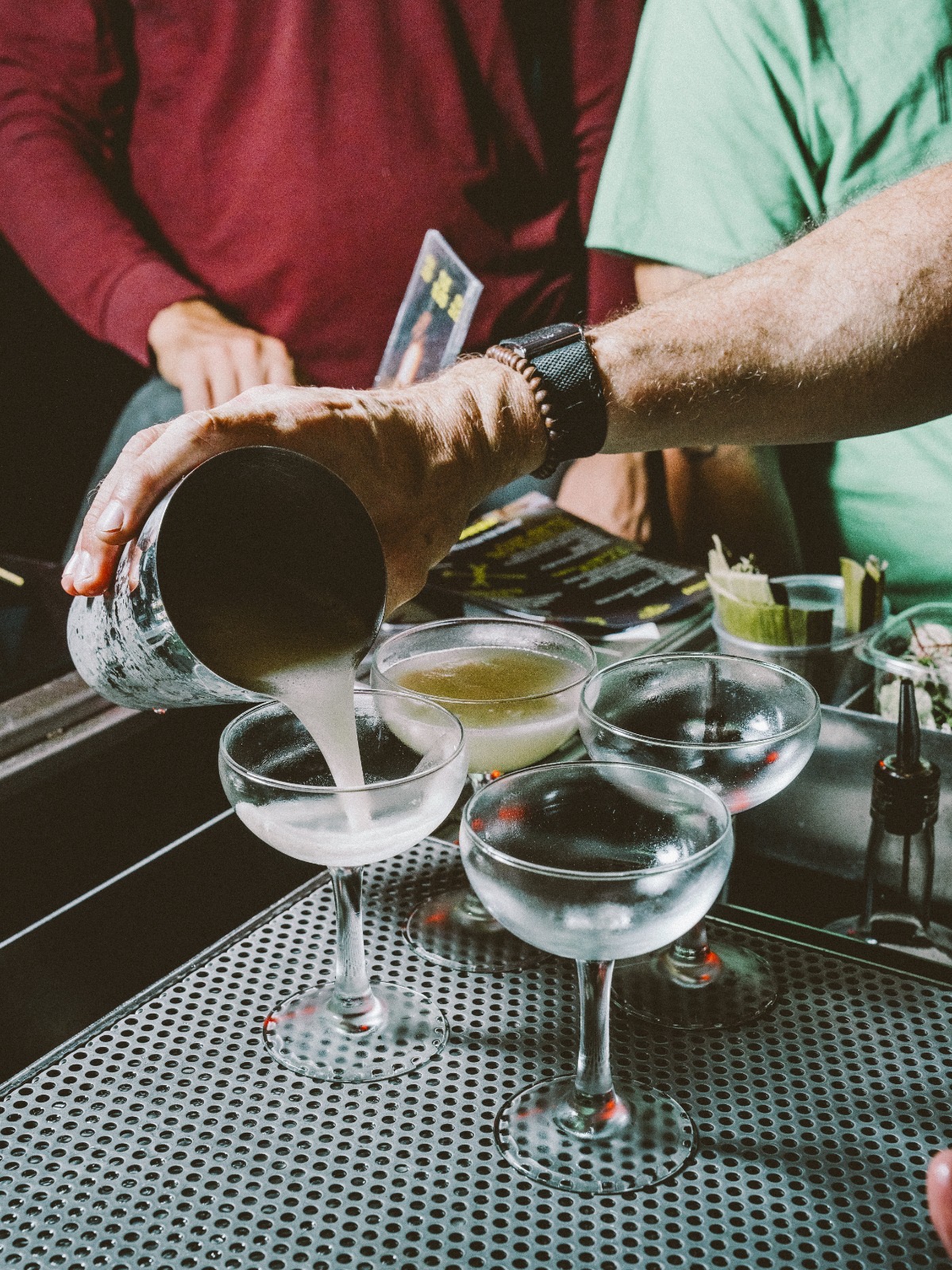 Préparation de cocktails au shaker, servis dans des verres à pied au bar.